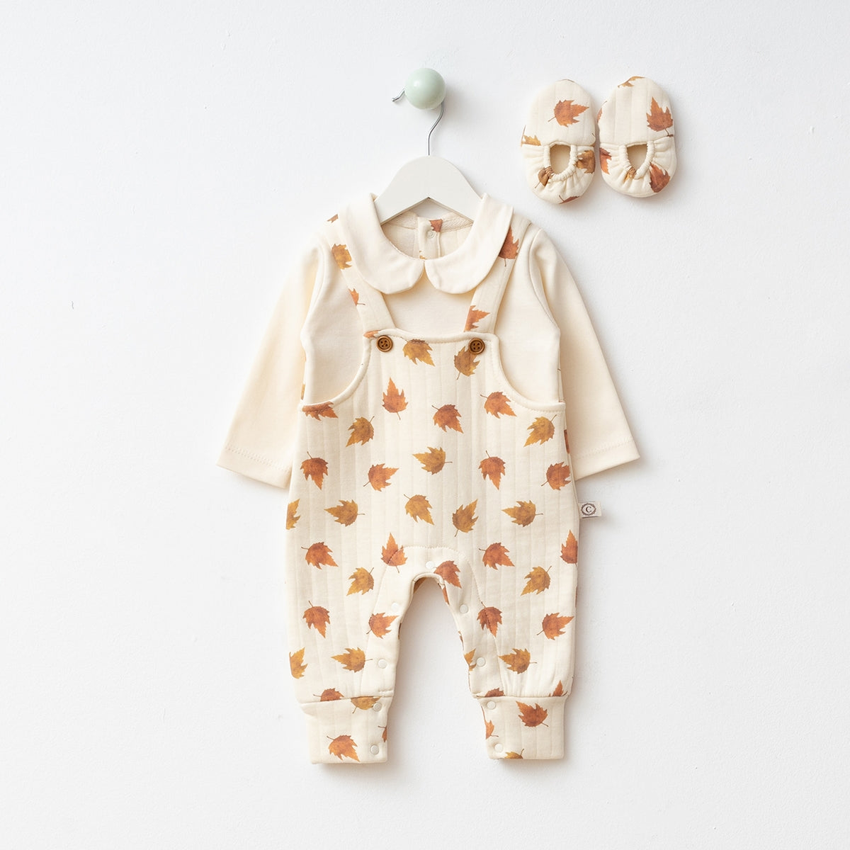 Cream baby onesie with leaf-patterned overalls and matching shoes