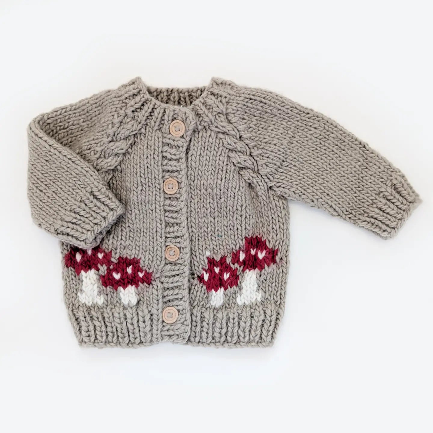 Hand-knitted beige baby cardigan with red and white mushroom pattern and wooden buttons.