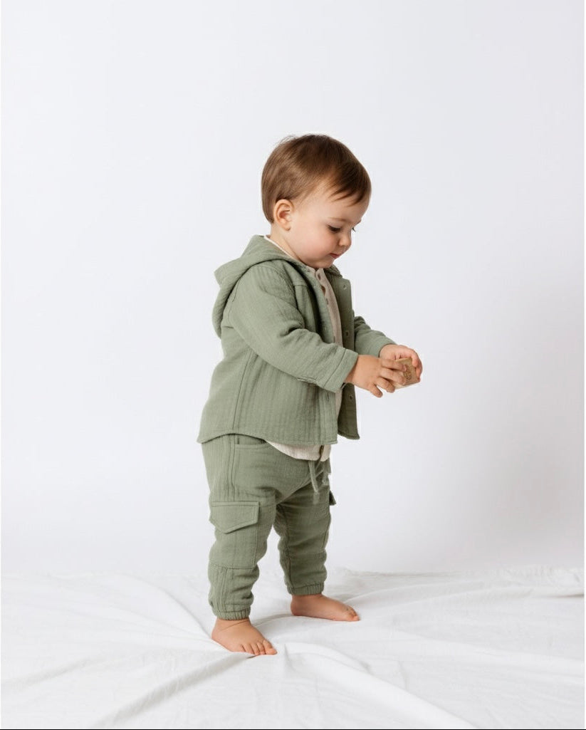 Sage green muslin baby outfit with hooded jacket, cream shirt, and pants.