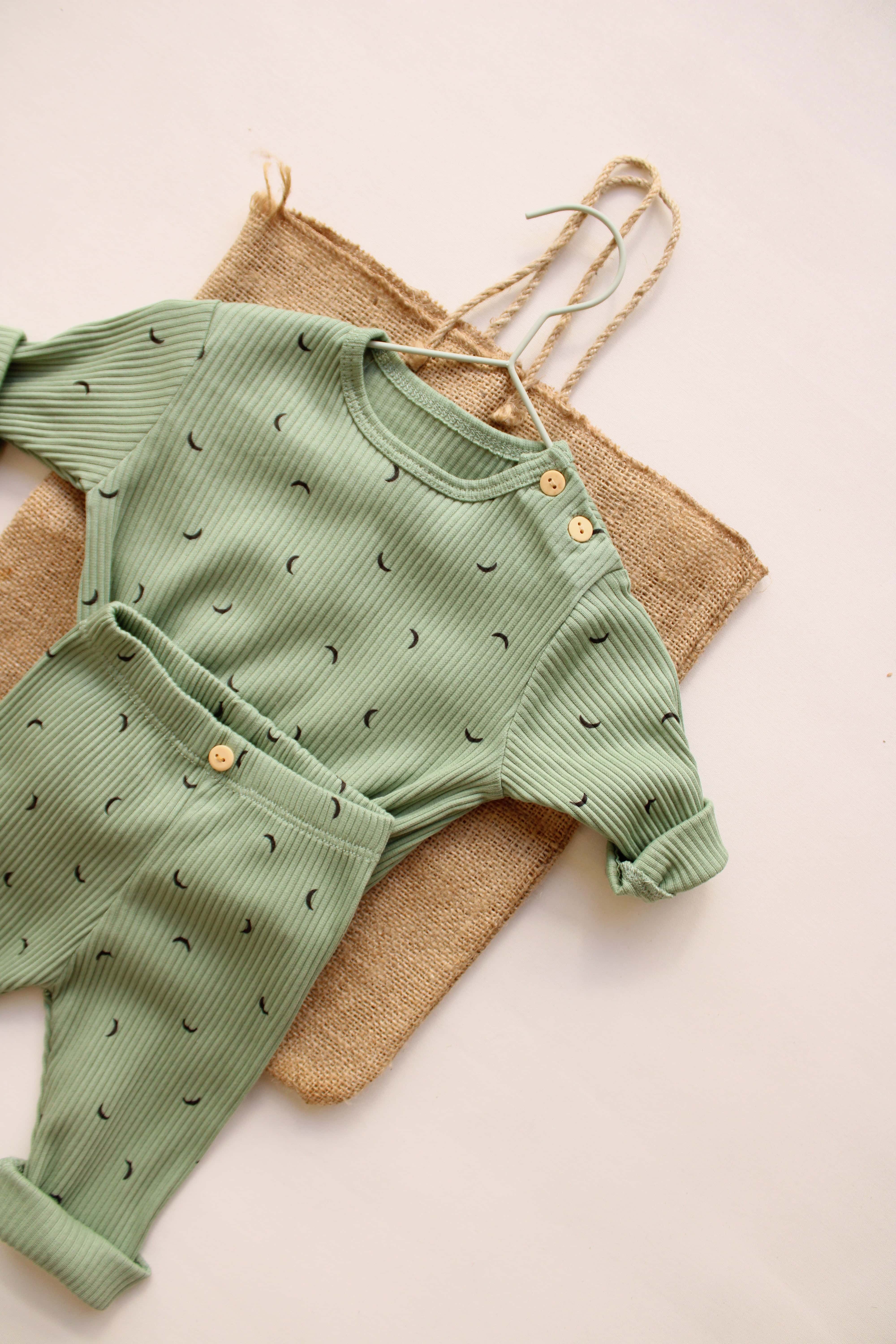 Green baby outfit with matching pants on a beige background