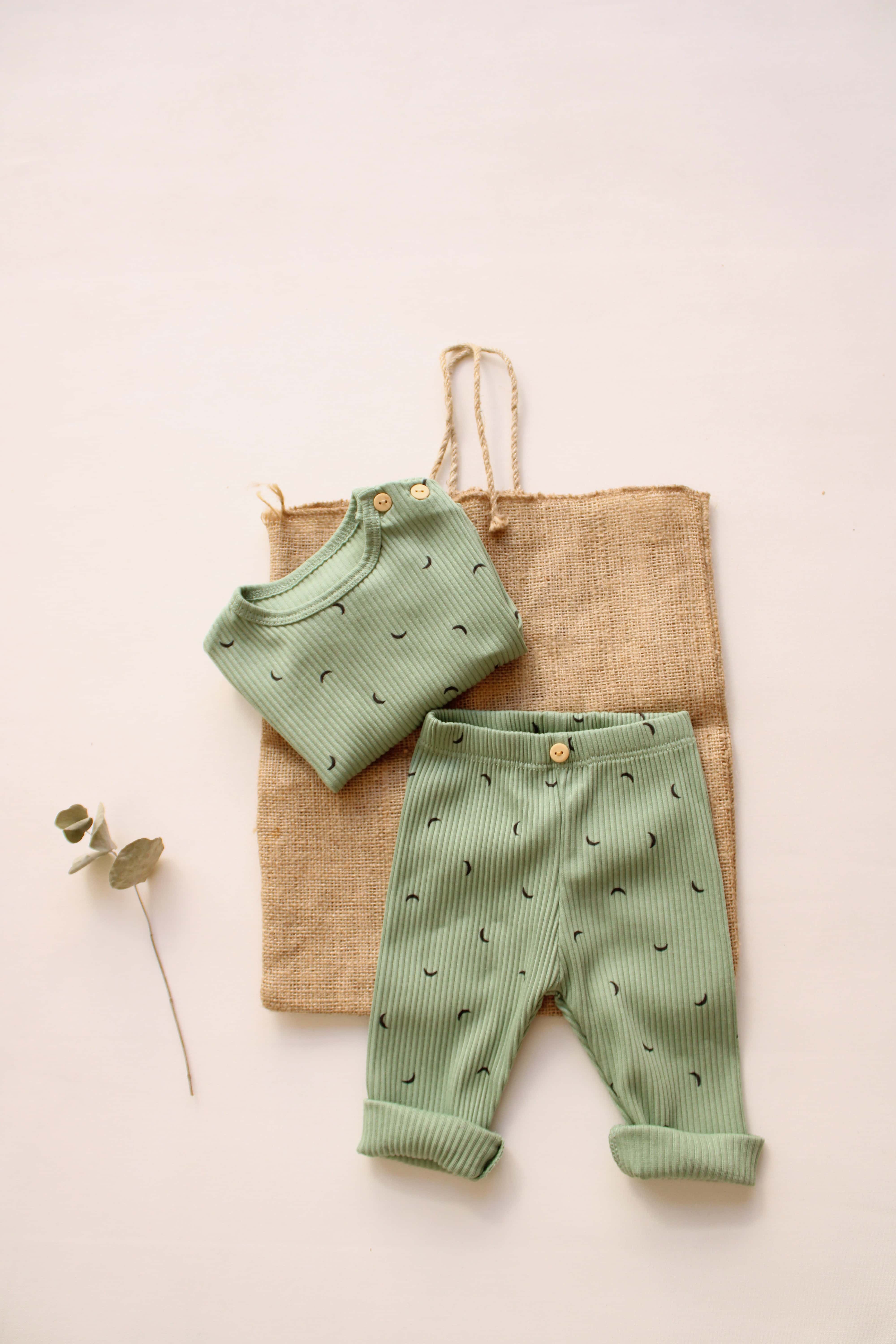 Green baby outfit with matching top and pants on a beige bag with a minimal background
