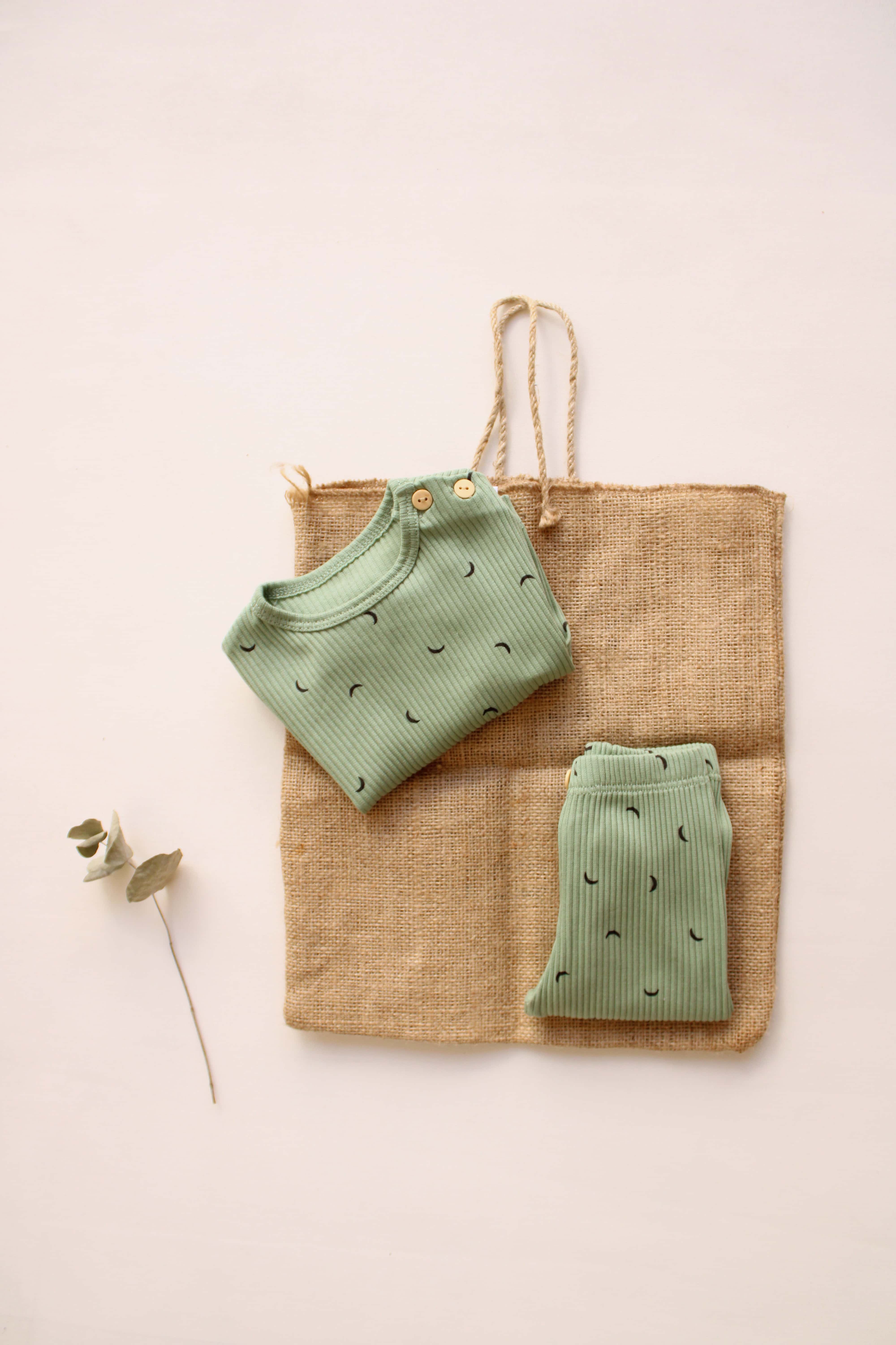 Two green baby rompers on a jute bag with a minimal background