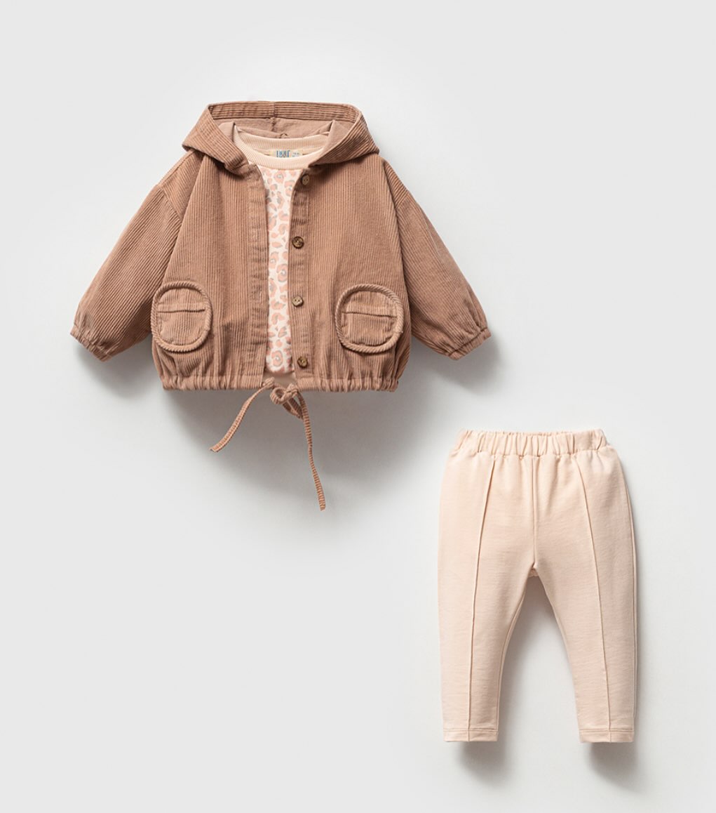 Beige baby outfit with corduroy jacket, printed top, and matching leggings.
