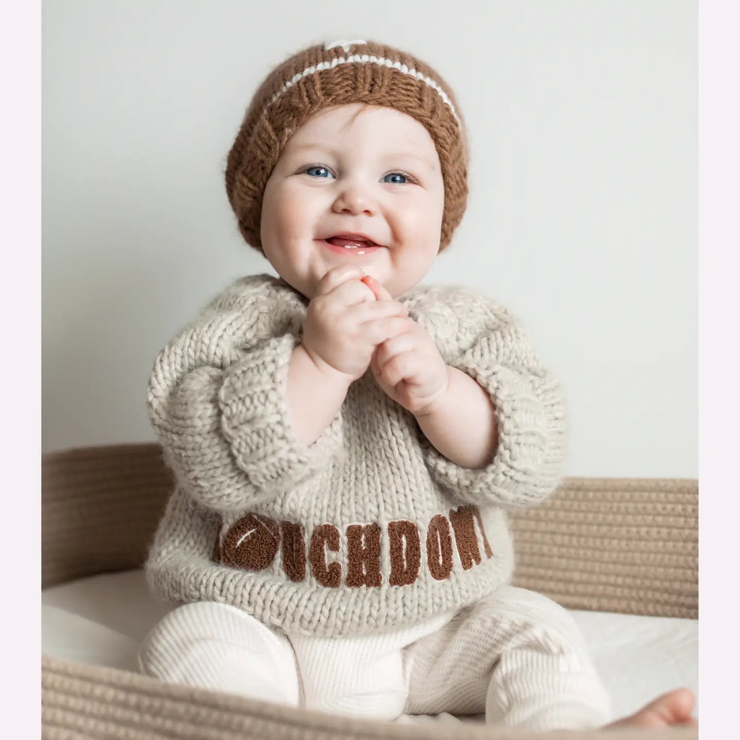 Baby wearing a knitted sweater and hat with 'OUCHDONT' text, sitting on a couch.