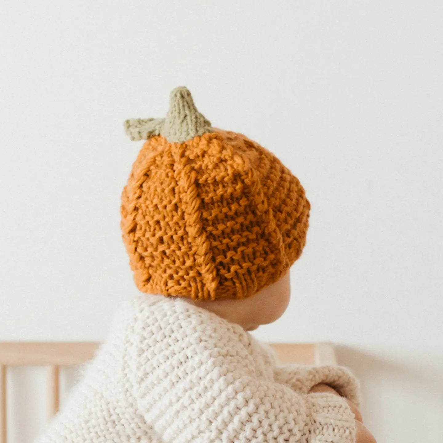 Baby wearing a knitted pumpkin hat with a neutral background