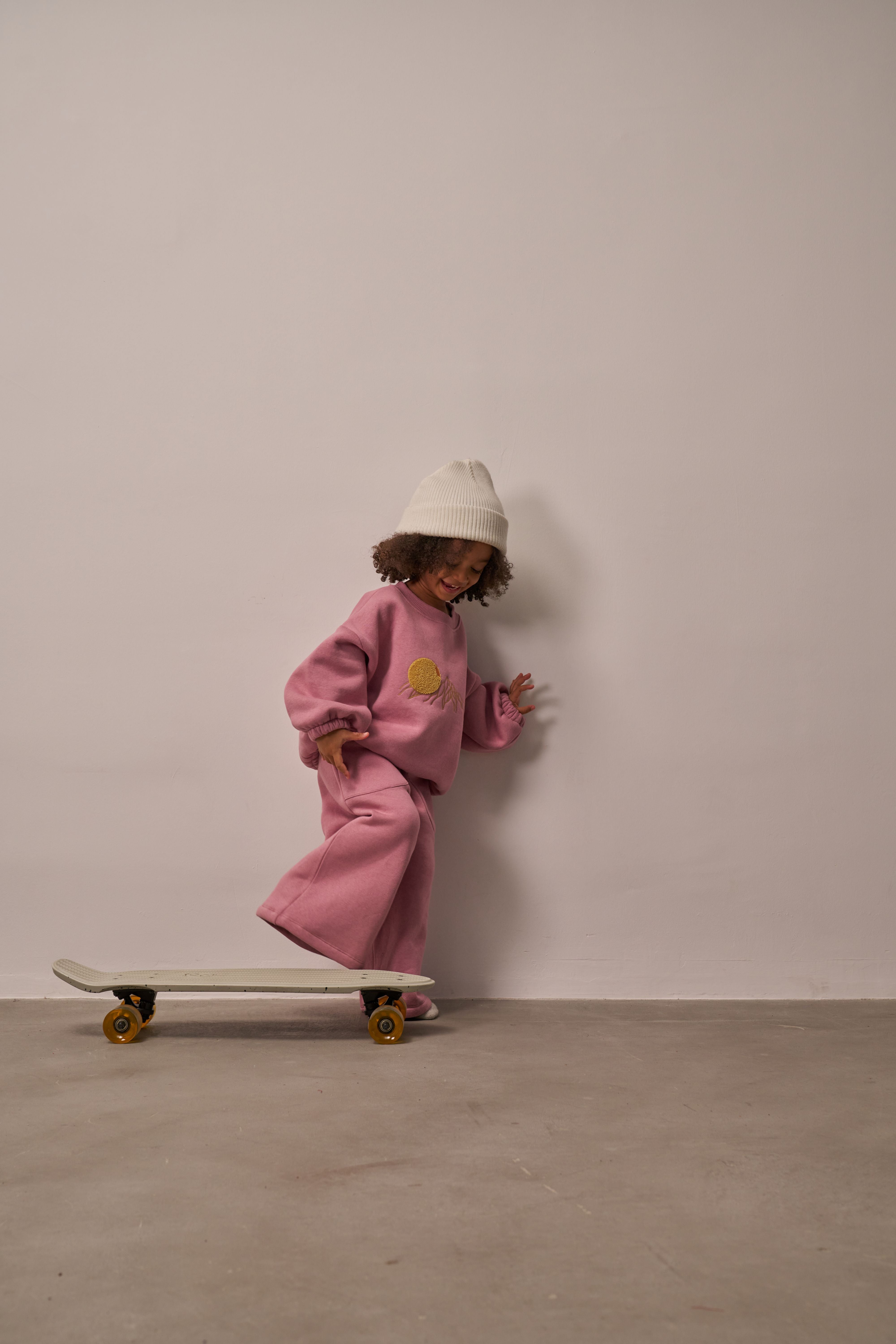 Child wearing soft pink loungewear set with sun embroidery on sweatshirt.