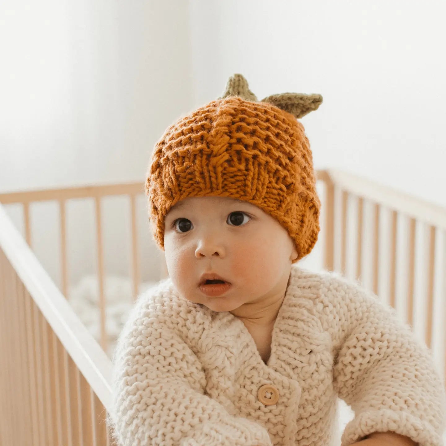 Baby wearing a knitted pumpkin hat in a crib