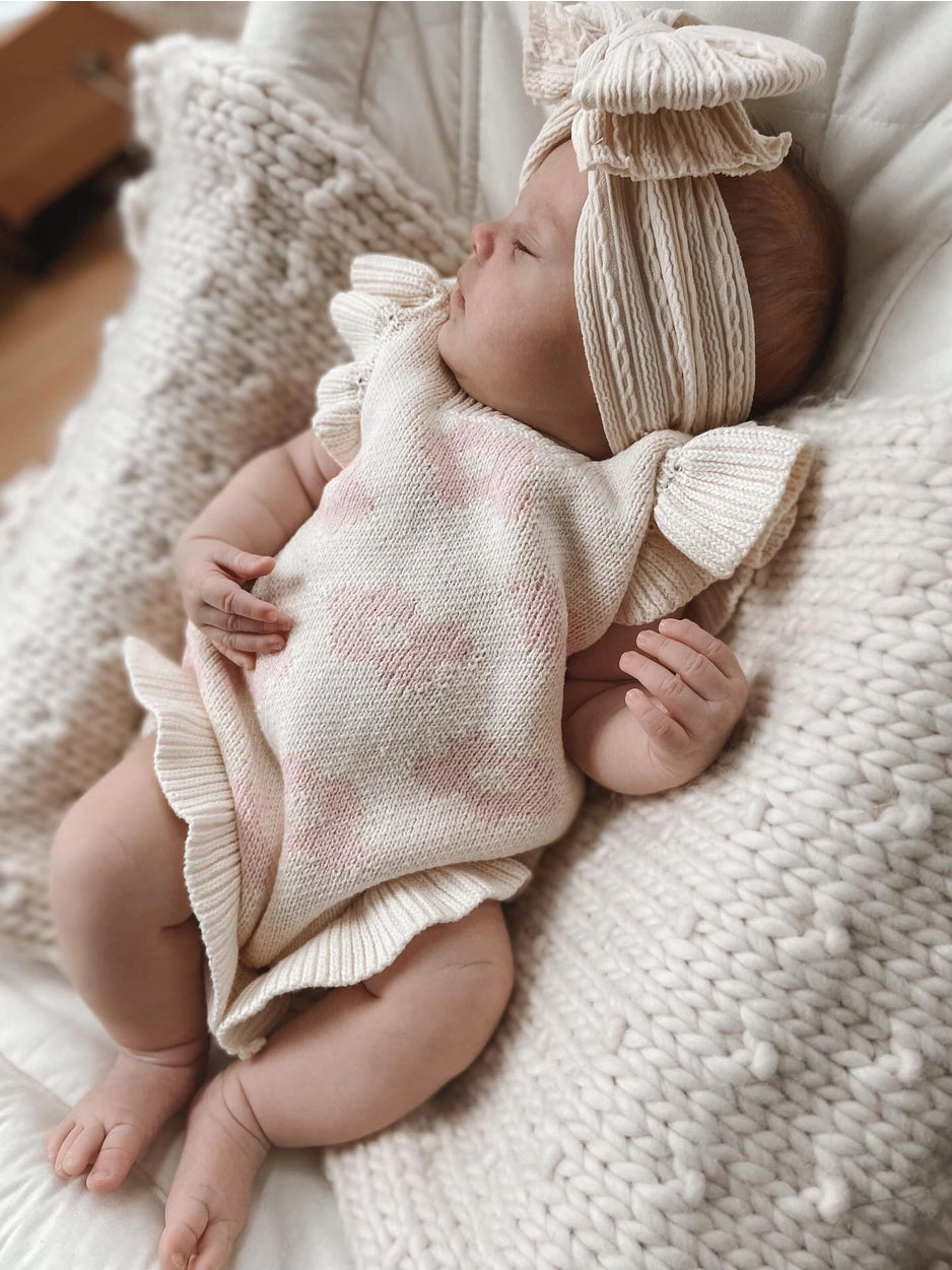 Newborn baby in a pink and white outfit with matching headband on a soft textured blanket.
