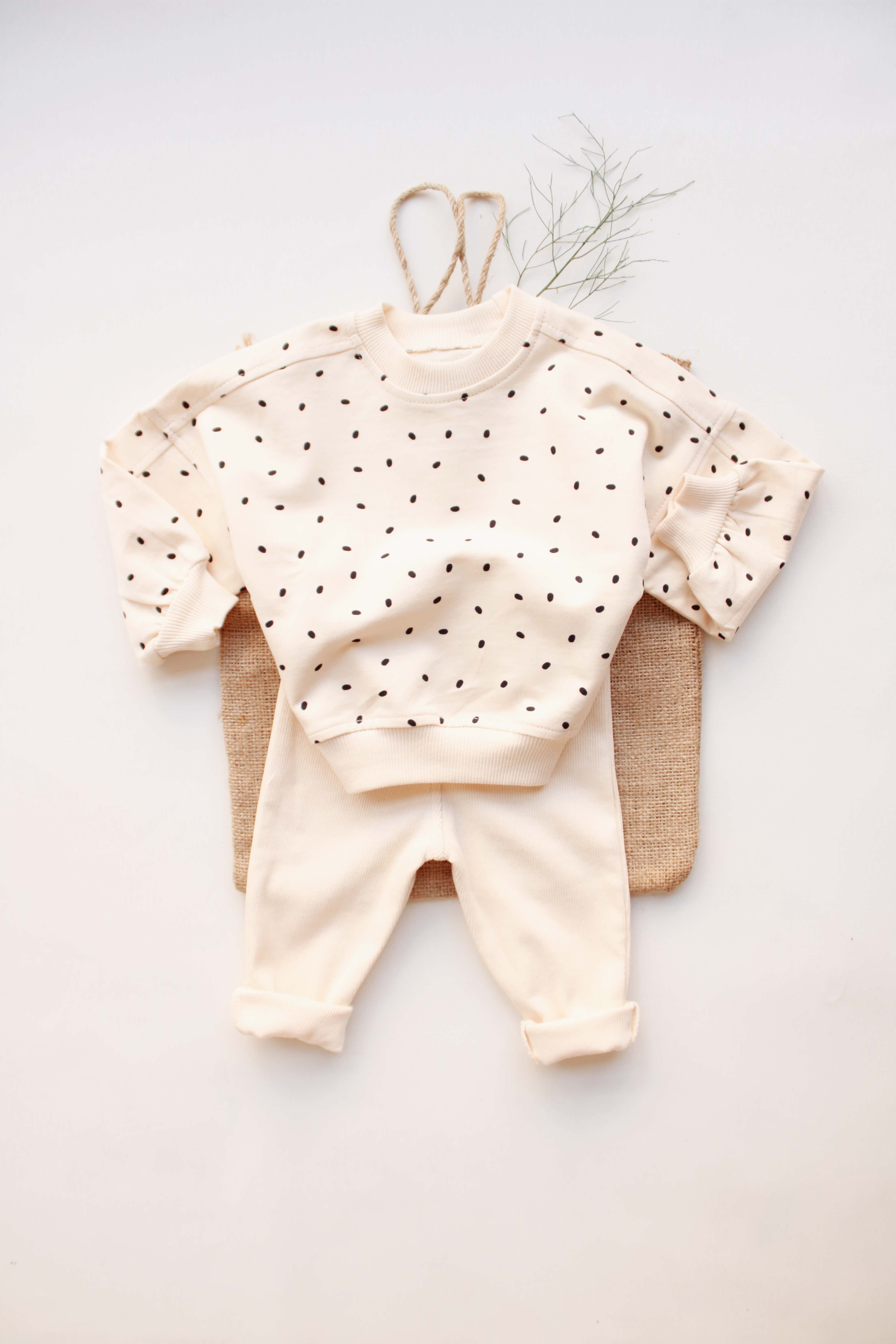 Beige baby outfit with black polka dots, sweatshirt, and matching pants.