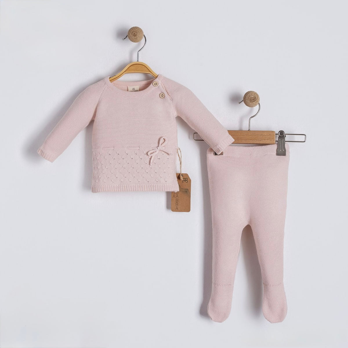 Baby sweater and pants set on hangers against a light gray background