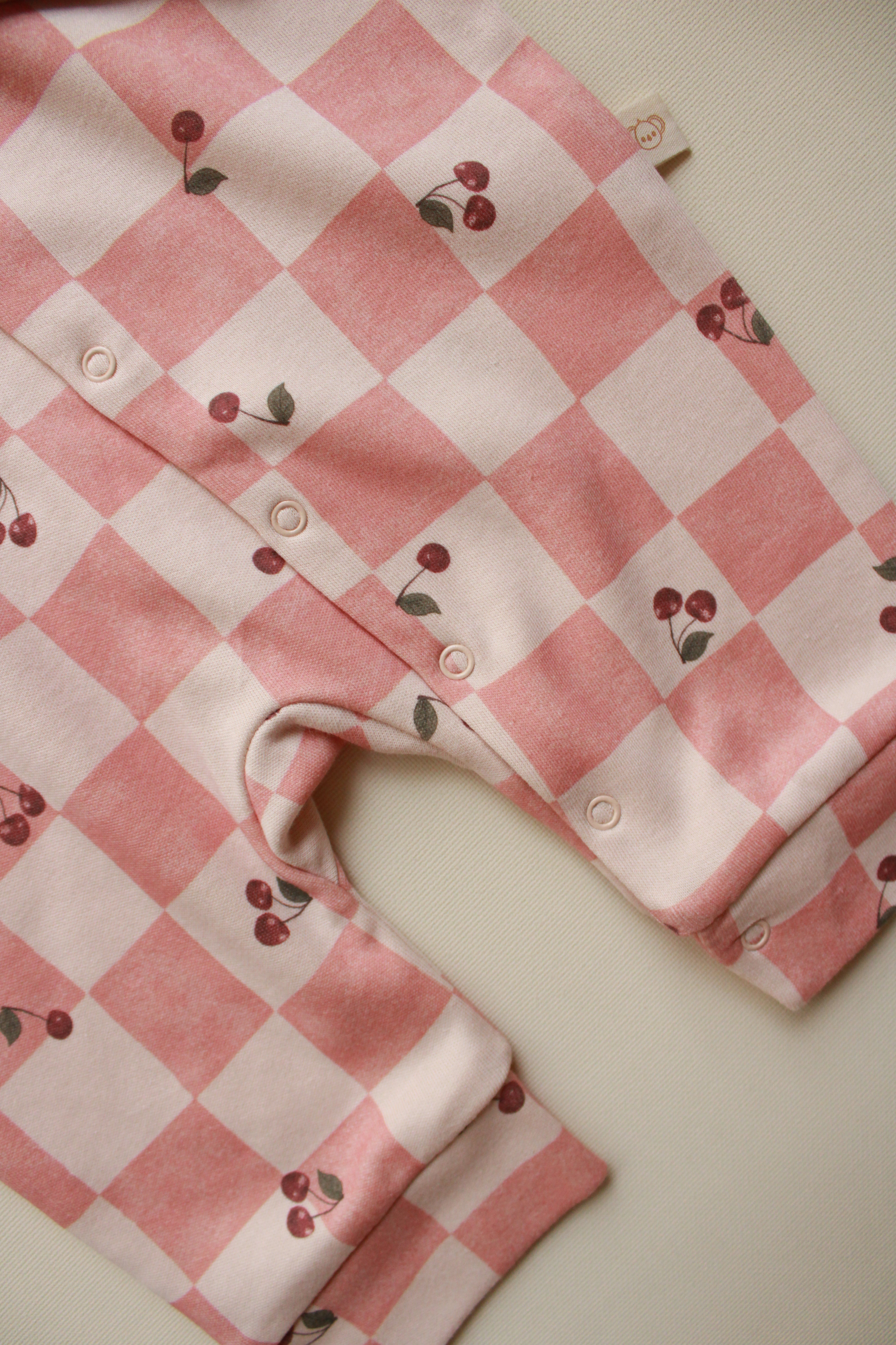 Pink and white checkered baby romper with cherry designs on a light background