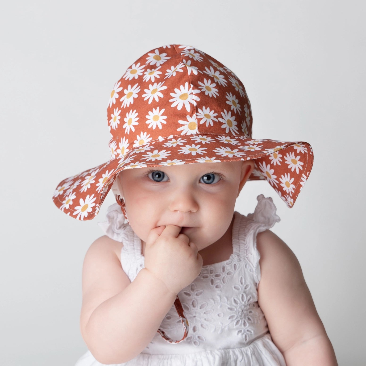 Baby wearing rust daisy print sun hat