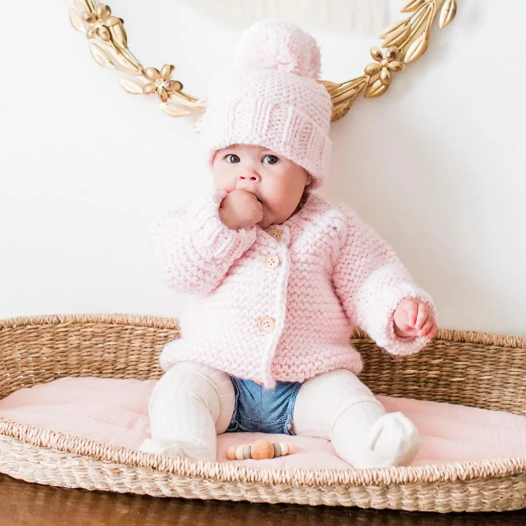 Cute knitted baby girl sweater in light blush pink, cozy handmade design with natural wooden buttons.