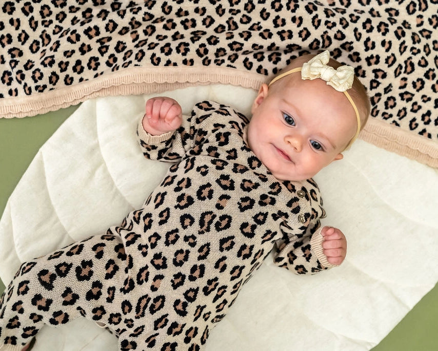 Close-up of leopard print baby jumpsuit featuring ribbed cuffs and wooden-style buttons